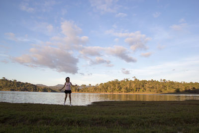 Full length of woman standing against lake and sky