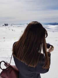 Rear view of woman photographing snow covered landscape through mobile phone