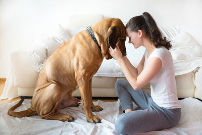 Side view of smiling young woman face to face with dog sitting at home