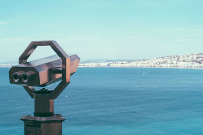 Close-up of coin-operated binoculars by sea against sky