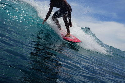 Low section of man surfing in the ocean against sky