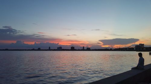 Silhouette city by sea against sky during sunset