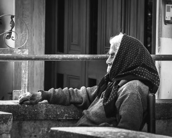 Senior woman sitting by retaining wall outside house