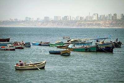 High angle view of fishing boats in water by buildings against sky