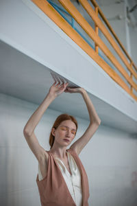 Young woman looking away while standing against wall