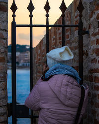 Rear view of woman standing by gate and wall in winter
