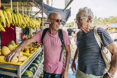 Smiling senior gay couple shopping fruits at greengrocer shop