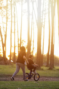 Mother helping son to ride bicycle during sunset