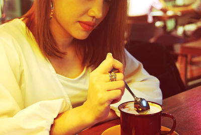 Midsection of woman stirring drink while sitting on table