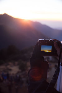 Man photographing at camera against sky during sunset