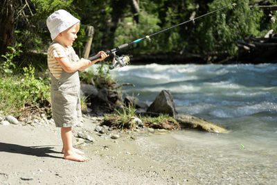 Little child boy fishing with a fishing rod on the mountain river on summer day