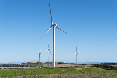 Windmills on field against clear blue sky