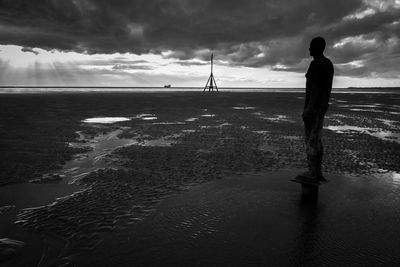 Man standing at beach against cloudy sky