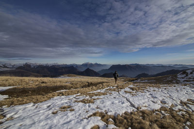 Rear view of hiker walking on snow covered field against sky