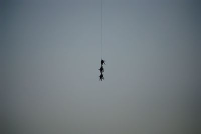 Low angle view of silhouette people hanging on rope against clear sky