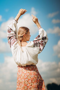 Rear view of woman with arms raised standing against sky