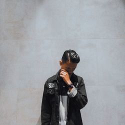 Young man looking away while standing against wall