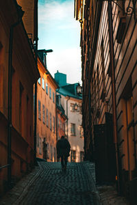 Rear view of man walking on street amidst buildings in city