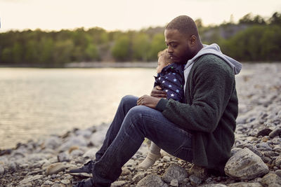 Side view of father sitting with baby boy on rocks at beach