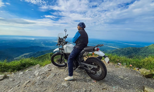 Young man biker sitting on bike at mountain top with mesmerizing view at morning