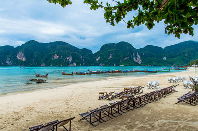 Chairs arranged on sand at beach against mountain