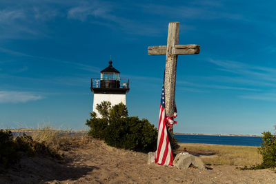 Cross by lighthouse on beach against blue sky