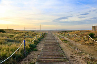 Boardwalk on field against sky during sunset