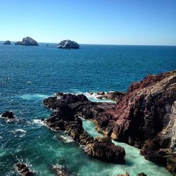 Rocks in sea against clear blue sky