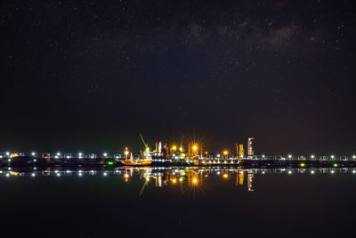 Illuminated buildings by lake against sky at night