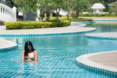 Smiling young woman sitting in swimming pool