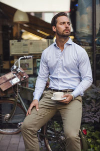 Thoughtful businessman holding coffee cup while sitting on bicycle at sidewalk cafe