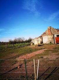 Plants growing on old building by field against blue sky