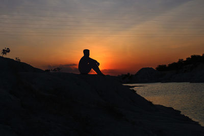 Silhouette man on rock against sky during sunset