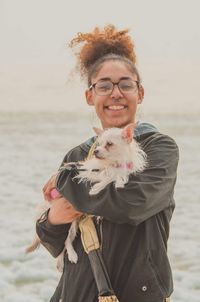 Portrait of smiling young woman with dog standing on beach