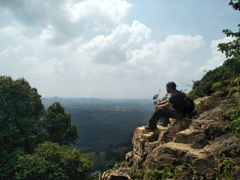 Man sitting on rock looking at mountains against sky