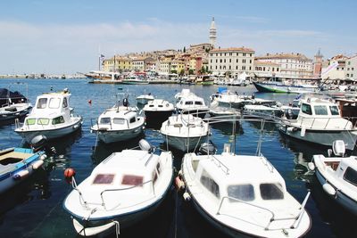 Boats moored at harbor by buildings against sky