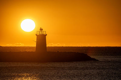 Lighthouse by sea against sky during sunset