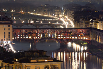 Illuminated bridge over river by buildings in city at night