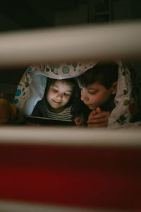 Siblings using digital tablet on bed in darkroom