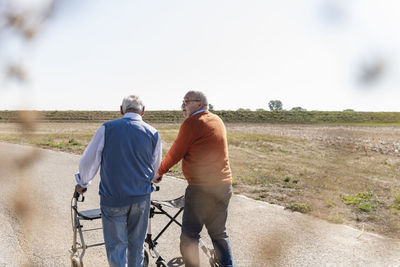 Two old friends walking on a country road, using wheeled walkers