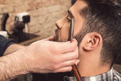 Cropped hands of barber trimming beards of man