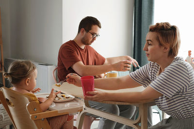 Parents with children having meal, breakfast by the table. mother serving food to family at home