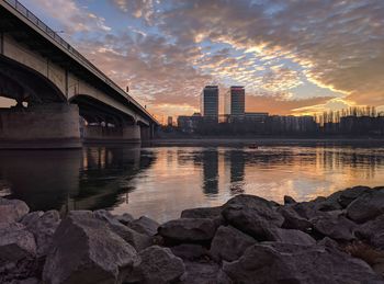 Bridge over river by buildings against sky during sunset