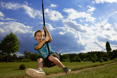 Full length of boy swinging over field against sky