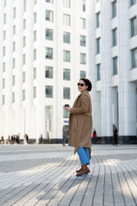 Full length of woman wearing sunglasses on footpath in city