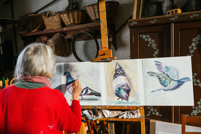 Back view of unrecognizable aged female artists in protective mask painting on canvas in backyard on sunny day in summer