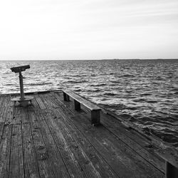 Binoculars by empty bench on pier over sea