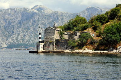 Lighthouse with stone structure on hill by sea and rocky mountain