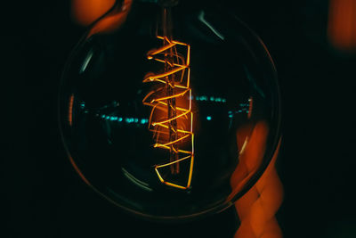 Close-up of hand holding illuminated glass against black background