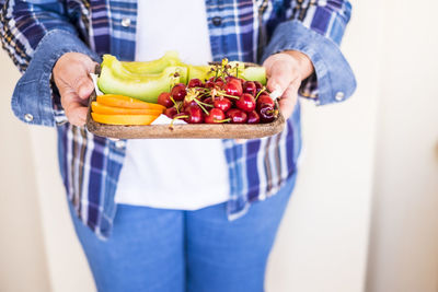 Midsection of woman holding fruits in tray at home